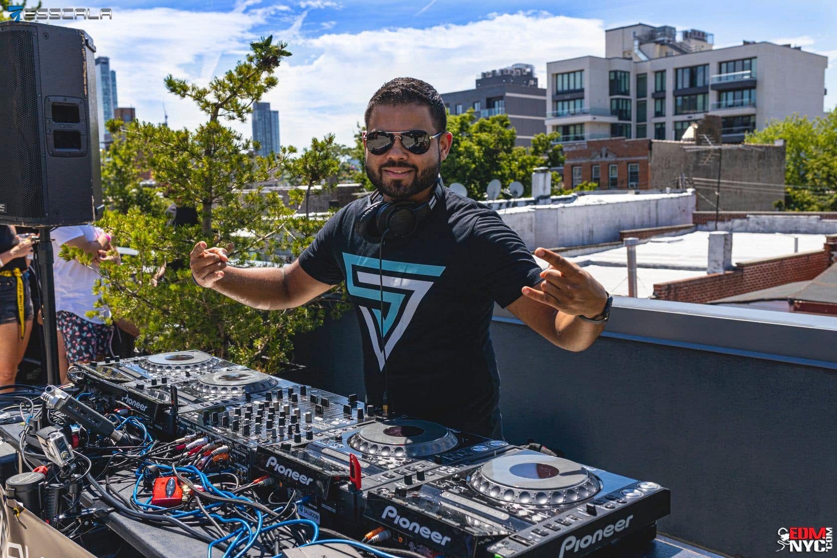 Sony Jacob smiling behind the decks at an outdoor rooftop party